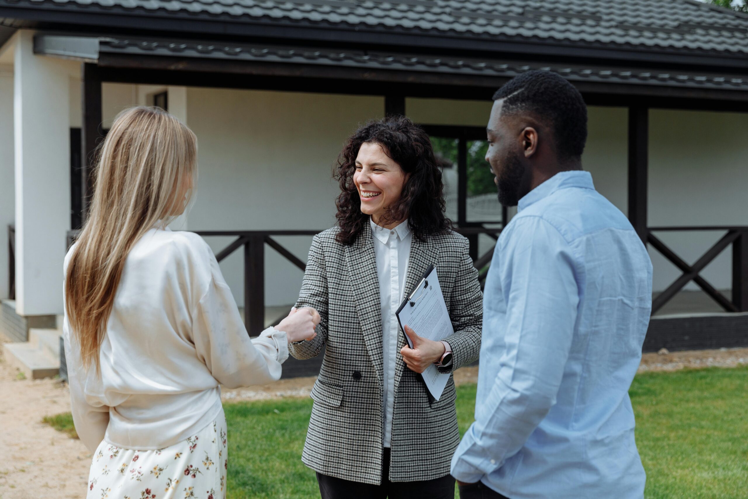 A smiling real estate agent shakes hands with a couple in front of a new home, symbolizing a successful homebuying experience